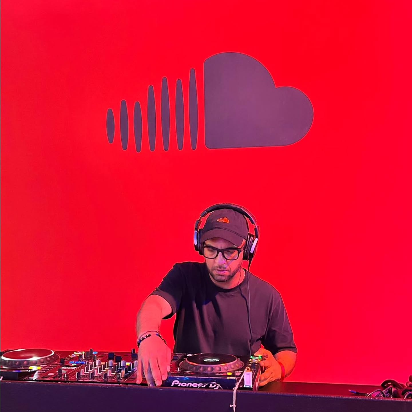 DJ Faraji mixing on Pioneer CDJs in front of a giant SoundCloud logo on a red wall
