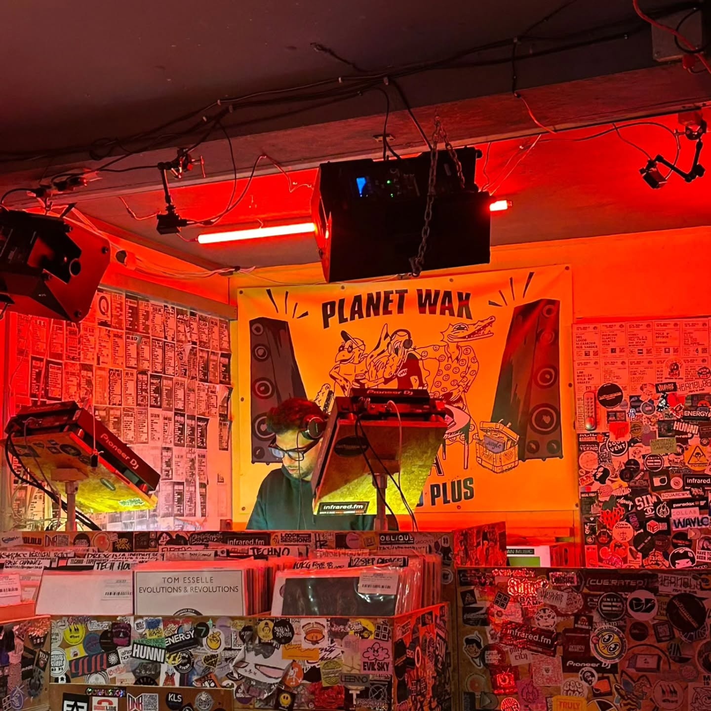 Red-lit Planet Wax booth in London with flyers, stickers and Pioneer DJ equipment